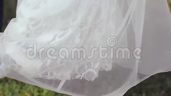 穿着白色连衣裙和白色鞋子的女孩在夏天公园的秋千上荡秋千春天视频的预览图