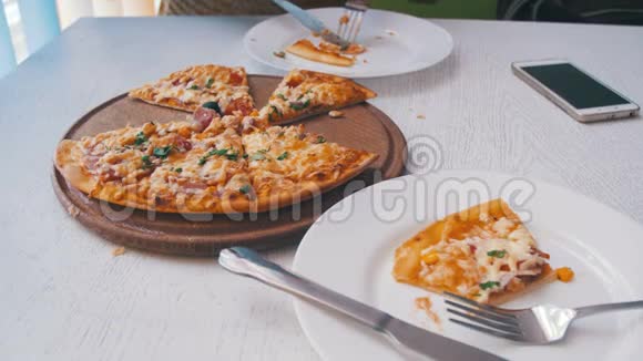 女人正在一家咖啡馆里吃披萨在白色时尚的木制桌子上放着手机视频的预览图