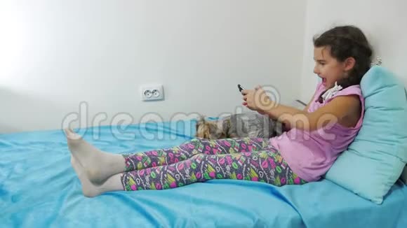健康技术和美容理念带智能手机的小女孩在床上和狗玩耍视频的预览图
