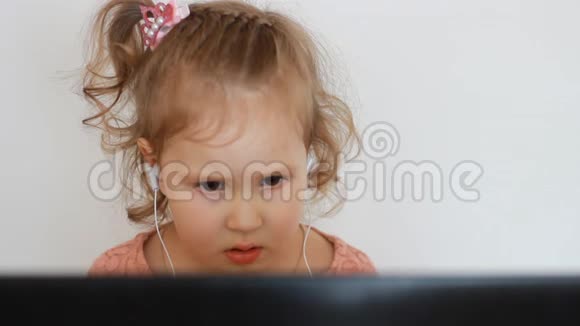 一个戴着耳机的小可爱女孩看着屏幕监视器电脑看电视录像卡通或玩游戏的滑稽儿童视频的预览图