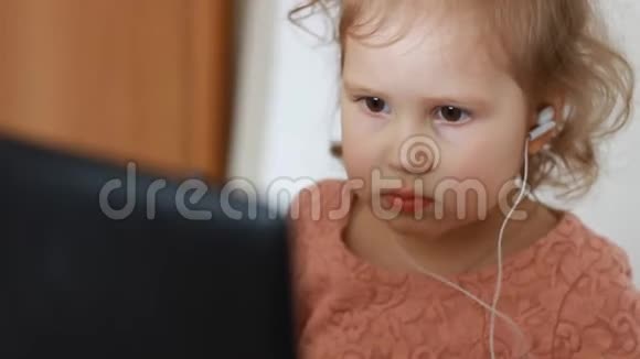 一个戴着耳机的小可爱女孩看着屏幕监视器电脑看电视录像卡通或玩游戏的滑稽儿童视频的预览图