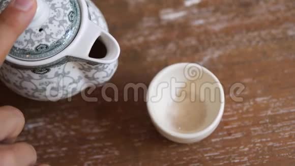 在木桌上用杯中的陈年茶点缓慢地饮用健康绿茶传统仪式视频的预览图