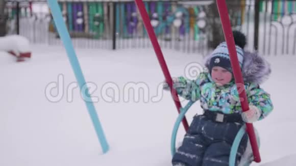 一个小孩子在冬天公园玩秋千上的一个孩子晴朗的冬日新鲜空气中的乐趣和游戏视频的预览图