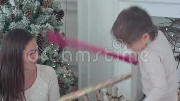快乐的母子在圣诞树附近打包纸剑视频的预览图