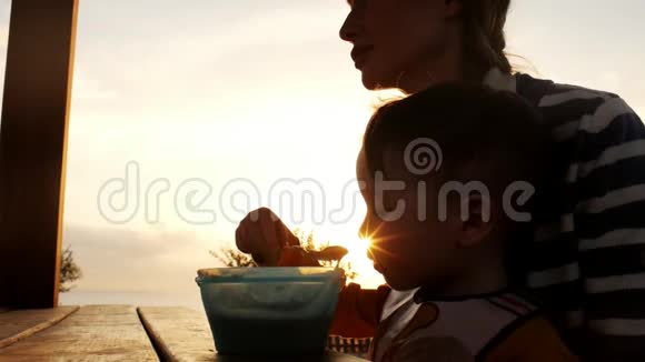 小男孩坐在妈妈腿上从婴儿食品盘中吃勺子视频的预览图
