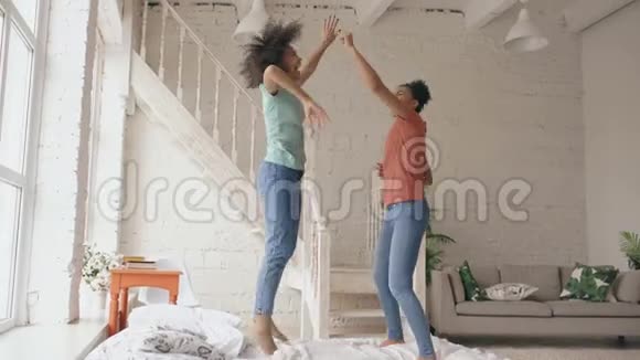 混合种族的年轻美丽的女孩在床上跳舞一起在家里的卧室里玩得开心视频的预览图