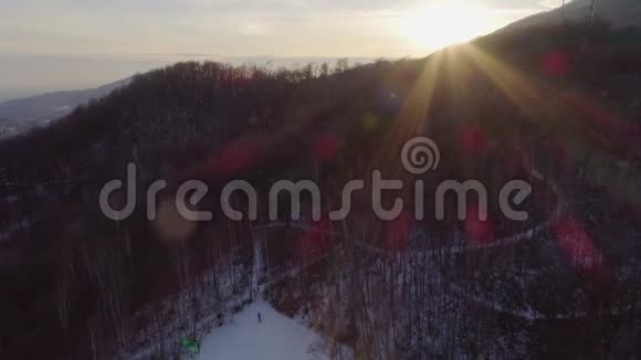 空中无人驾驶飞机在日落时分飞过白雪皑皑的森林人们在散步户外山地冬季雪视频的预览图