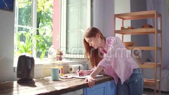 年轻女子在厨房里用笔记本写字视频的预览图
