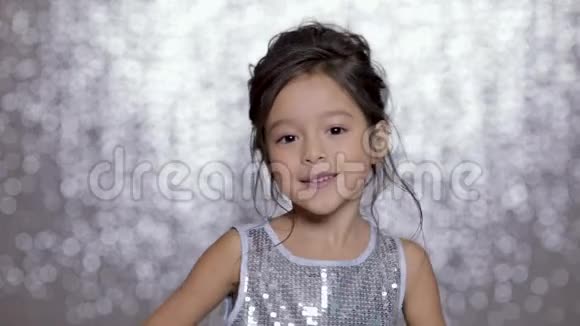 美丽的微笑的小女孩穿着银色的裙子在银色的背景下跳舞视频的预览图