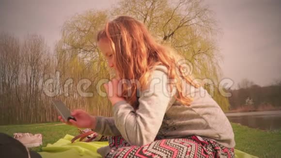 那个可爱的少女坐在公园的草地上拿着一部智能手机视频的预览图