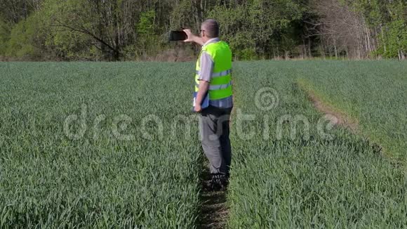 农夫在智能手机上拍照在绿色的谷物场上散步视频的预览图