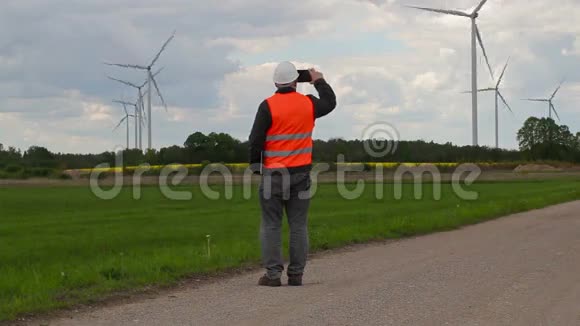 电动工程师在风车附近的智能手机上行走和拍照视频的预览图