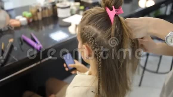 女孩在理发师使用智能手机而理发师则在客户的头发上工作视频的预览图