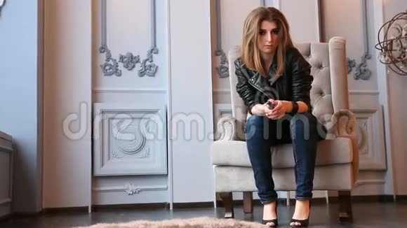 时尚棕色头发的女人坐在豪华扶手椅皮夹克和牛仔牛仔裤上视频的预览图
