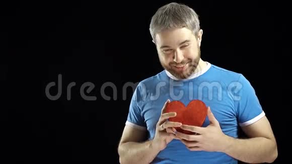 穿着蓝色t恤的满脸胡须的男人手里拿着两个红色的心形爱情浪漫约会关系概念黑色视频的预览图