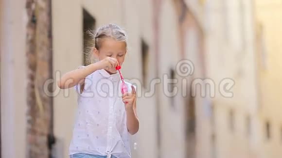 在欧洲城市的狭窄街道上吹肥皂泡的小女孩白种人儿童享受暑假的肖像视频的预览图