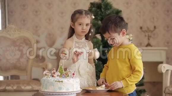 小女孩和男孩在圣诞树的背景上吃蛋糕带圣诞树的大客厅视频的预览图