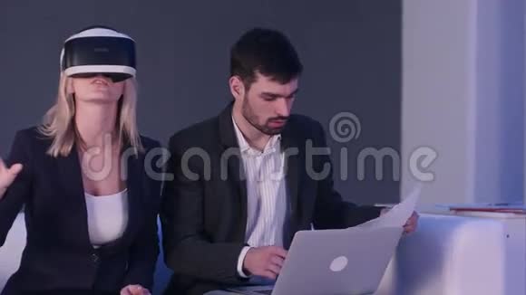 戴着vr耳机的金发女人和她的伴侣在笔记本电脑前拿着蓝图讨论建筑项目视频的预览图
