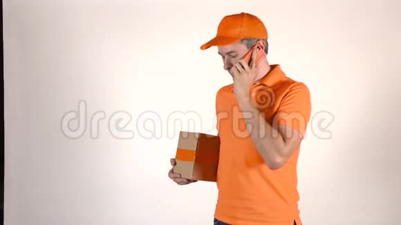 穿着橙色制服的英俊的快递员在他的手机上交谈送了一个包裹浅灰色背景4K演播室视频的预览图