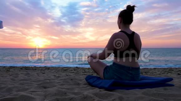 日出时在海滩上练习瑜伽的年轻女子视频的预览图