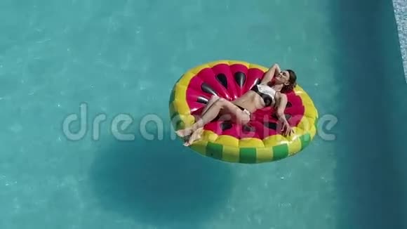 穿着泳衣的空中女孩在一个西瓜形状的充气床垫上日光浴深色晒黑视频的预览图