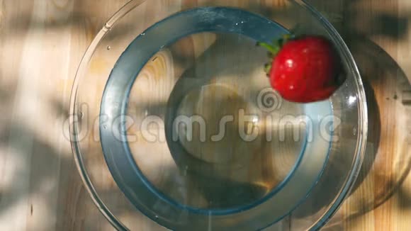 成熟的新鲜草莓落在水碗站在木桌上慢速运动靠近俯视图视频的预览图