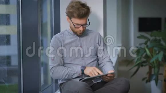 年轻的商人坐在窗边浏览视频的预览图