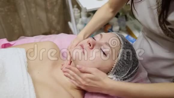 有魅力的女性在水疗健康俱乐部得到面部按摩美容师按摩面部颈部和肩部视频的预览图