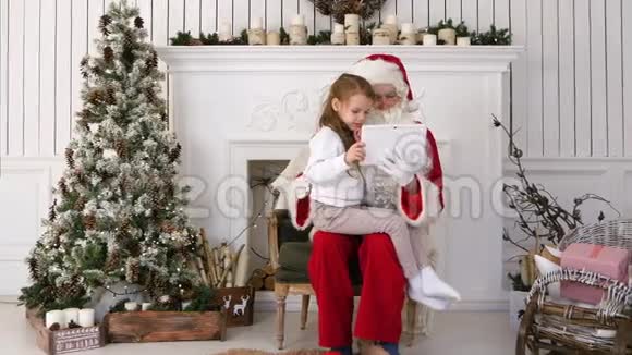 坐在严肃圣诞老人面前的小女孩用平板电脑视频的预览图