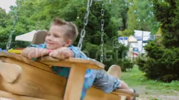 微笑的男孩在操场上玩得很开心夏天孩子们在户外玩耍在外面骑着秋千的少年视频的预览图