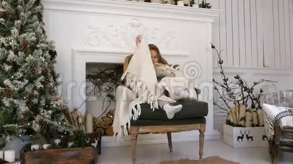 小女孩坐在圣诞树附近的椅子上手里裹着一条毯子视频的预览图