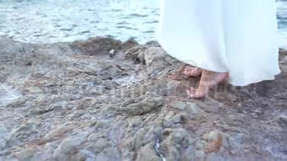 穿着白色衣服的漂亮女孩站在海边的石头上希腊视频的预览图