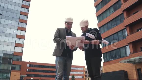 施工现场的领班和建筑师两个戴着建筑头盔的人在建筑地点讨论计划视频的预览图