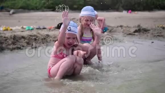 两个女孩在海滩上泼水在炎热的夏日里双胞胎倒着水孩子们的笑声和好心情视频的预览图