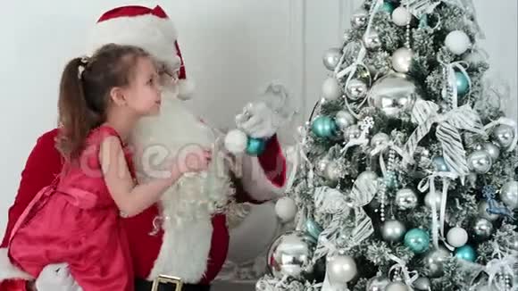 假圣诞老人装饰圣诞树抱着一个小女孩的胳膊视频的预览图