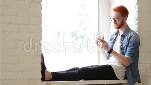 使用智能手机坐在窗口人w红发和胡子视频的预览图