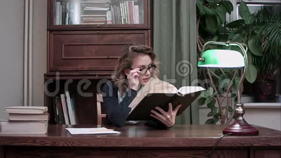 戴眼镜的年轻聪明的女人拿着一本书热情地读书视频的预览图