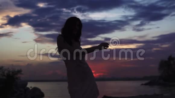 日落天空背景下穿着鸡尾酒礼服的女孩剪影美丽的女孩跳舞在上面玩得开心视频的预览图