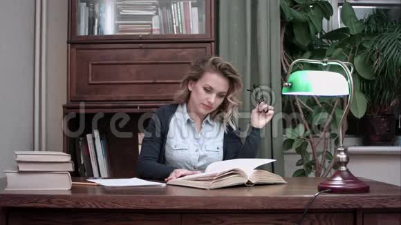一个微笑的女人坐在办公桌前愉快地翻阅着一本书视频的预览图