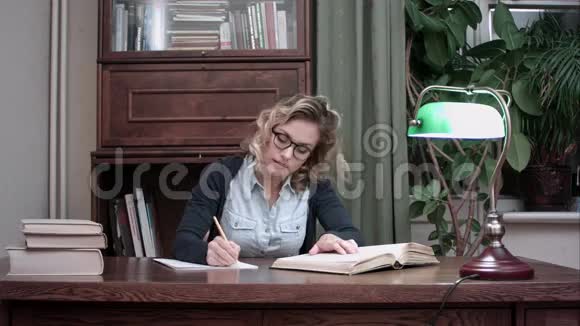 戴眼镜的年轻学生坐在桌子旁从书上写笔记视频的预览图