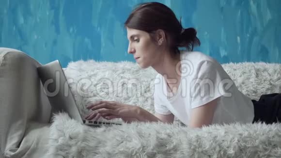 在家里躺在沙发上用笔记本电脑的女人视频的预览图