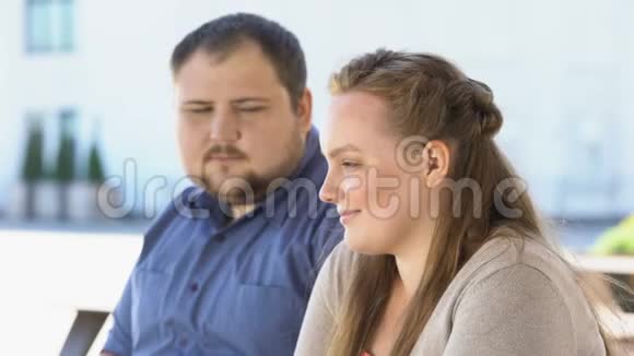 年轻人抱着女朋友坐在长凳上在公园里浪漫约会胖子夫妇视频的预览图