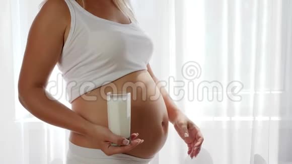 怀孕的女性表现出相似的认可并在大肚子的背景下持有玻璃牛奶奶制品视频的预览图