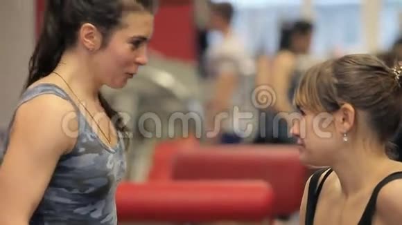 两个女人在健身房锻炼后放松和交谈两个女孩在健身房聊天女孩们在运动机器之间大笑视频的预览图