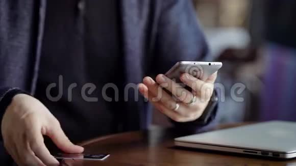 关闭男性手键入智能手机塑料卡号咖啡馆里的年轻人在现代的帮助下付账视频的预览图