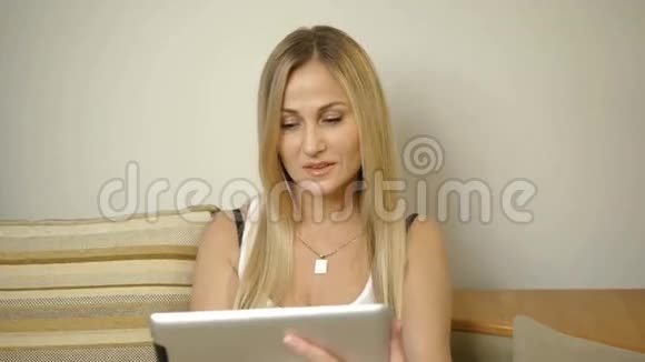 家里的女人拿着信用卡和平板电脑在沙发上视频的预览图