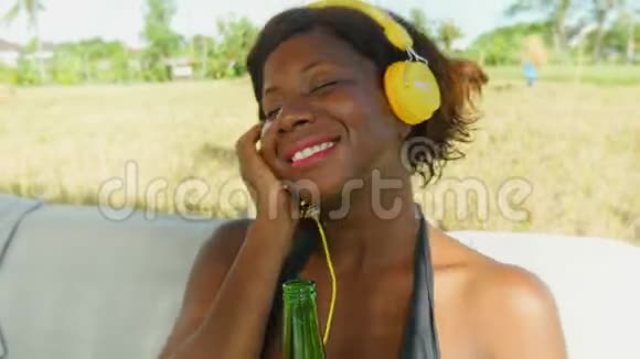 快乐的黑色非洲美国女人带着耳机听着户外音乐冰镇着轻松享受暑假视频的预览图