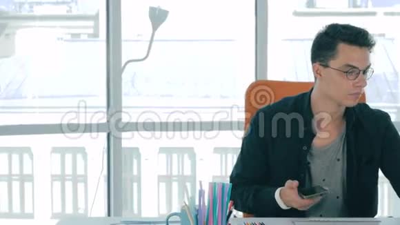 英俊的设计师坐在创意办公室使用智能手机视频的预览图