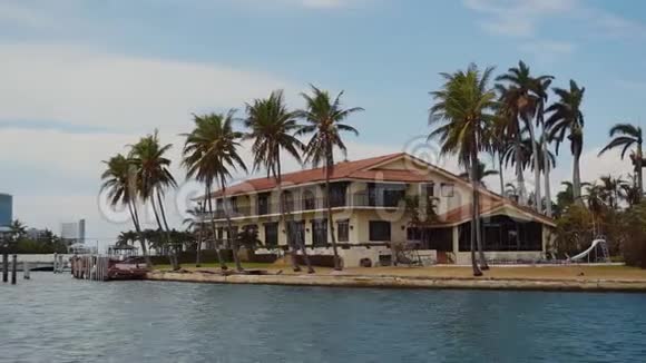 迈阿密阳光明媚的小岛海滩蓝天白云下海湾岸边棕榈树丛中的豪华豪宅视频的预览图