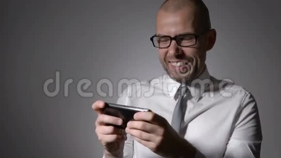 非常有表现力和情感的经理穿着白色衬衫和领带在他的智能手机上玩游戏视频的预览图